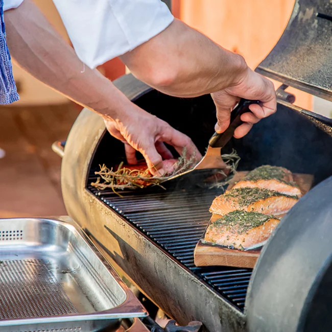 Person legt Lachsfilets mit Kräutern auf einen Grill