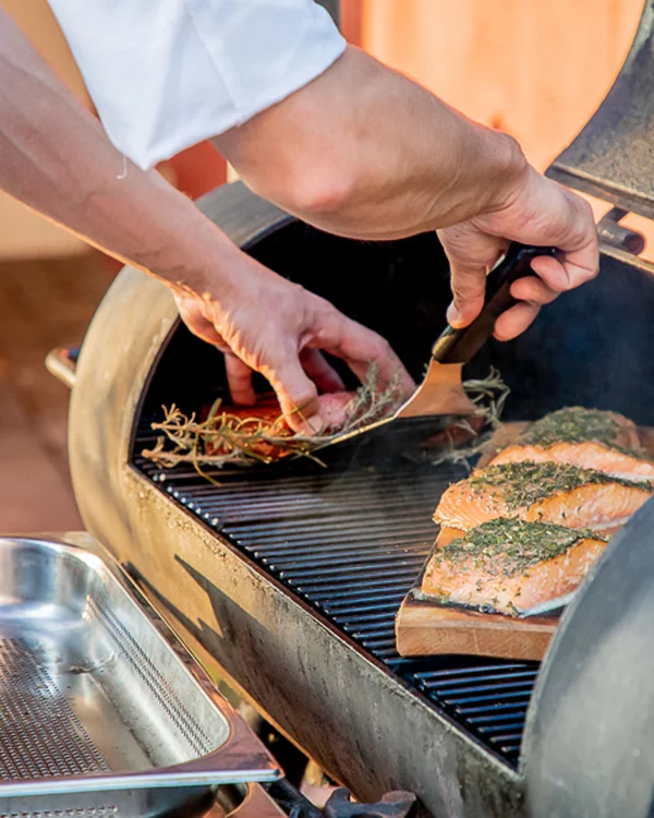 Person legt Lachsfilets mit Kräutern auf einen Grill