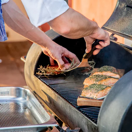 Person legt Lachsfilets mit Kräutern auf einen Grill