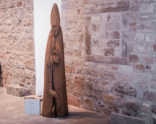 Holzfigur eines bischöflichen Heiligen mit Kreuz in einem Museum