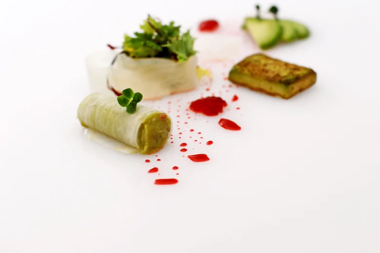 Kreativ angerichtetes Gourmetgericht auf weißem Teller mit Gemüse und roten Soßentropfen