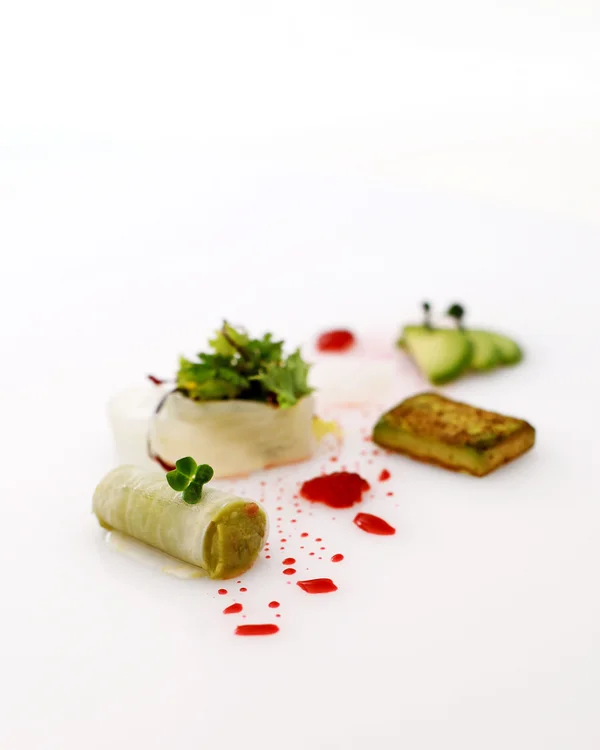 Kreativ angerichtetes Gourmetgericht auf weißem Teller mit Gemüse und roten Soßentropfen