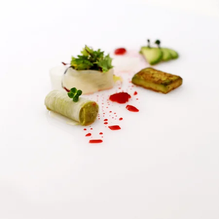 Kreativ angerichtetes Gourmetgericht auf weißem Teller mit Gemüse und roten Soßentropfen