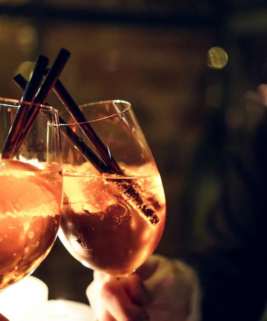 Zwei Gläser mit orangenfarbenem Getränk und schwarzen Strohhalmen bei Kerzenlicht