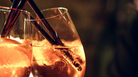 Zwei Gläser mit orangenfarbenem Getränk und schwarzen Strohhalmen bei Kerzenlicht