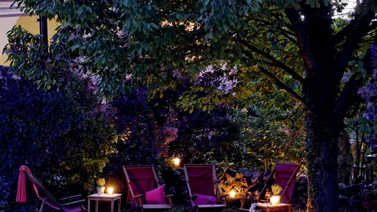 Abendliche Gartenbeleuchtung mit Stühlen und Kerzen unter einem Baum