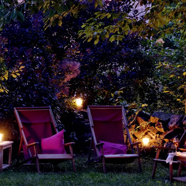 Abendliche Gartenbeleuchtung mit Stühlen und Kerzen unter einem Baum