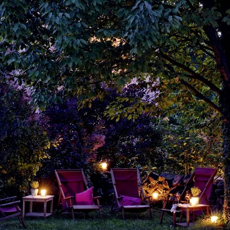 Abendliche Gartenbeleuchtung mit Stühlen und Kerzen unter einem Baum