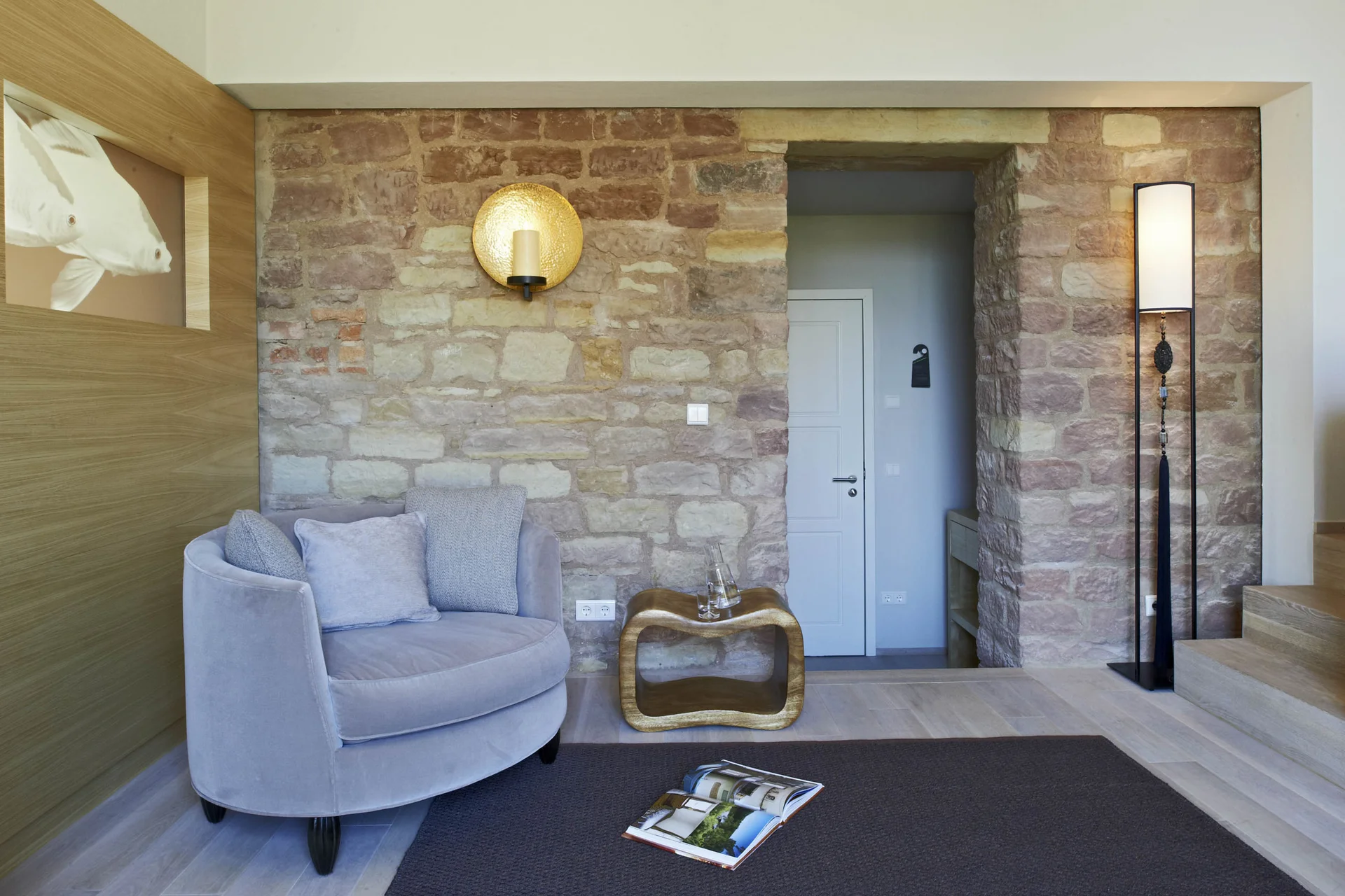 Gemütliche Sitzecke mit grauem Sessel, goldenem Beistelltisch und Steinwand