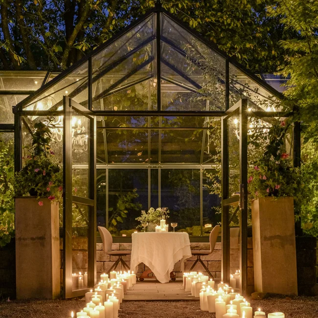 Glashaus mit Kerzen beleuchtet, Weg führt zum gedeckten Tisch