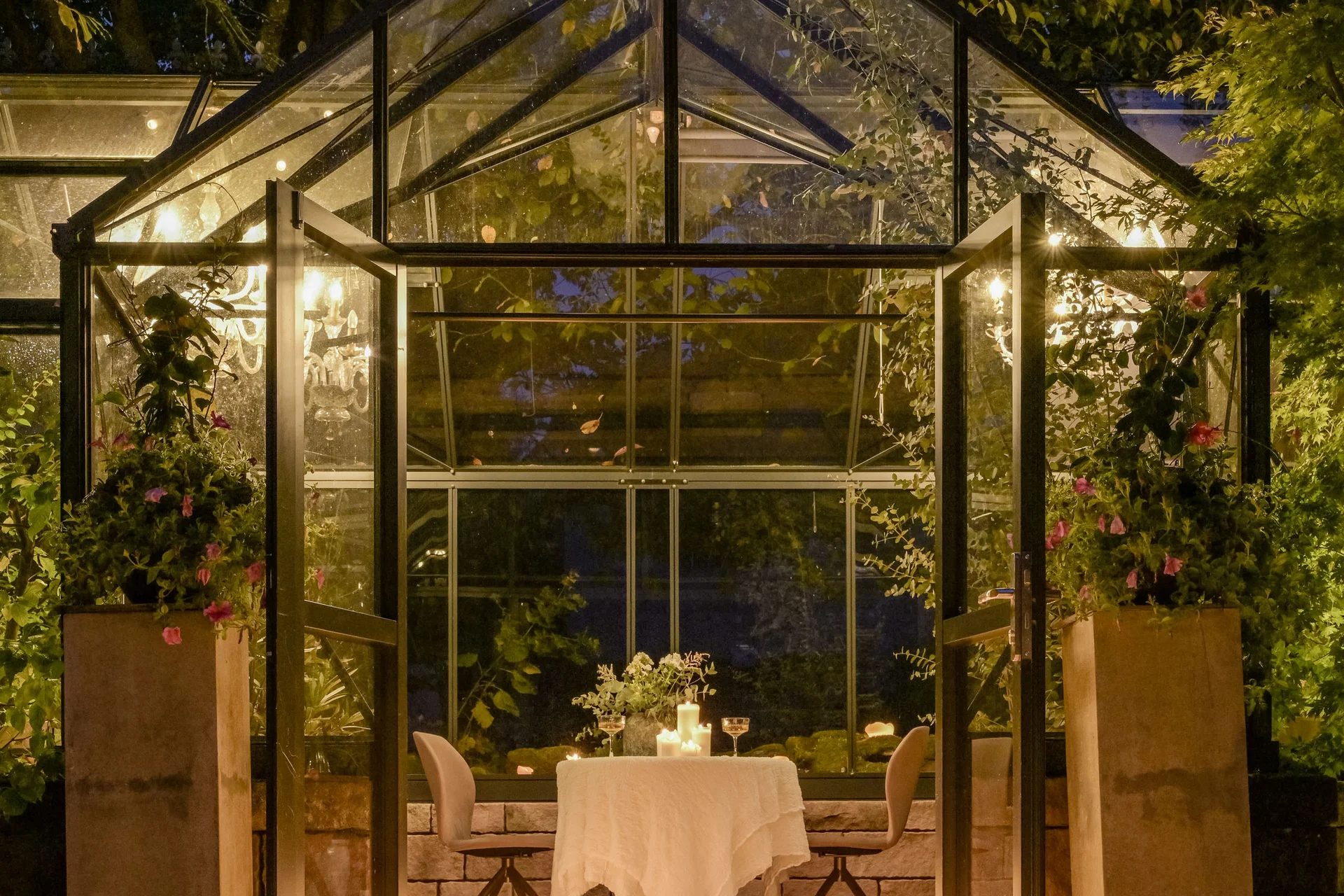 Glashaus mit Kerzen beleuchtet, Weg führt zum gedeckten Tisch