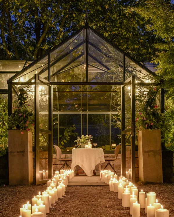 Glashaus mit Kerzen beleuchtet, Weg führt zum gedeckten Tisch