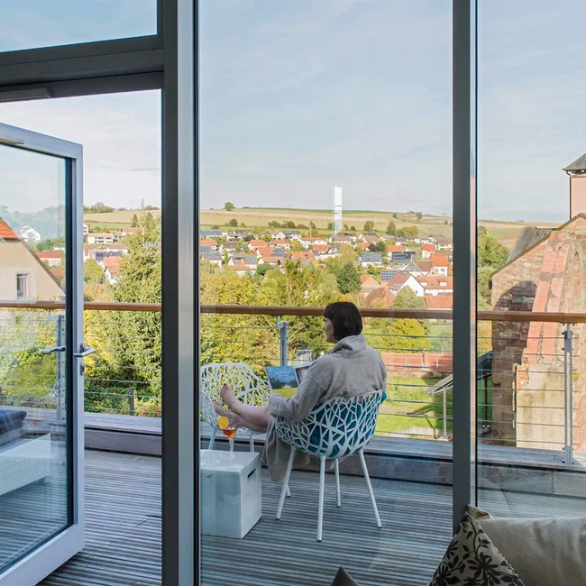 Person liest auf Balkon mit Blick auf Kirche und Dorf im Hintergrund
