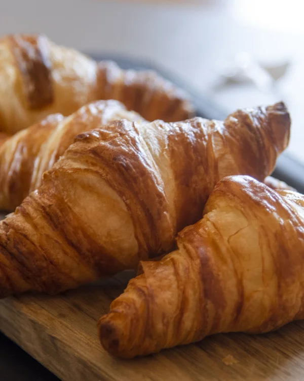 Drei frische Croissants auf einem Holzbrett neben einem Glas mit Trauben