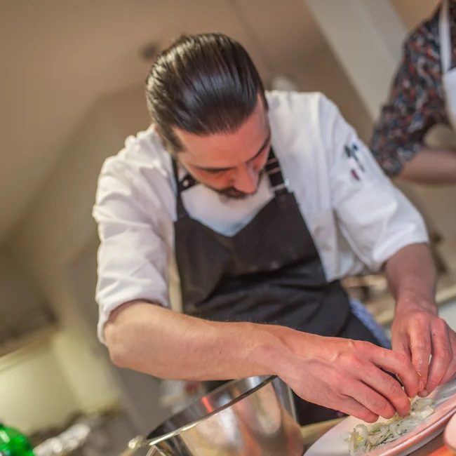 Koch richtet sorgfältig ein Gericht auf einem Teller an