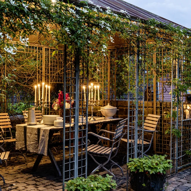 Abendessen im Gartenpavillon mit Kerzenlicht und blühenden Pflanzen