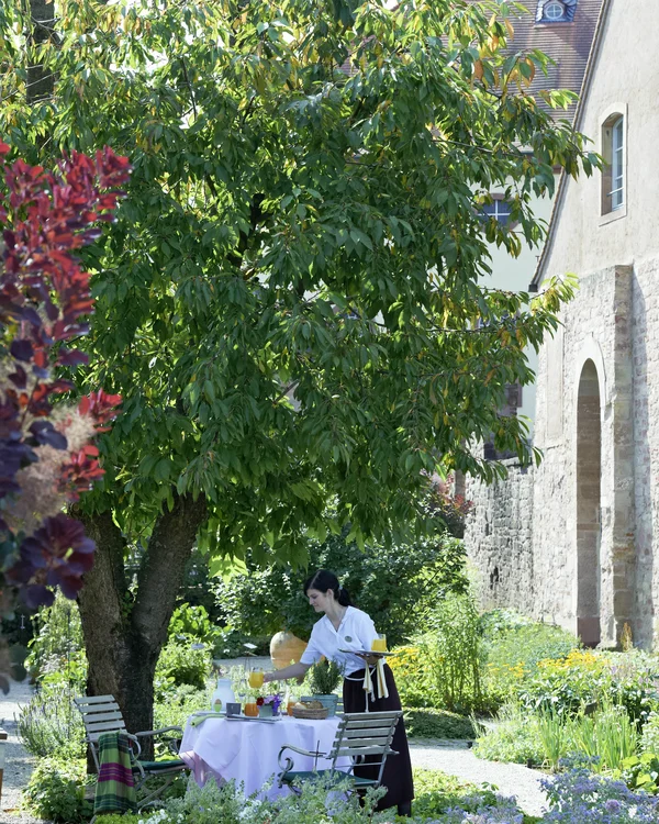 Kellnerin deckt Tisch im Garten neben altem Gebäude an sonnigem Tag