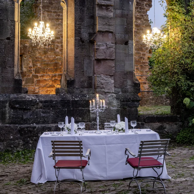 Beleuchteter Esstisch mit Kerzen in Ruinen eines alten Steinbaus bei Dämmerung