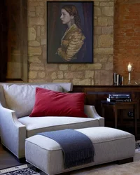 Sitzbereich mit grauem Sofa, rotem Kissen und Gemälde an Steinwand