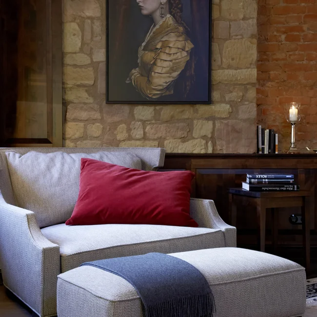 Sitzbereich mit grauem Sofa, rotem Kissen und Gemälde an Steinwand