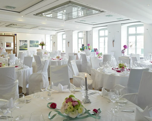 Eleganter Hochzeitssaal mit weiß gedeckten Tischen und Blumendekoration