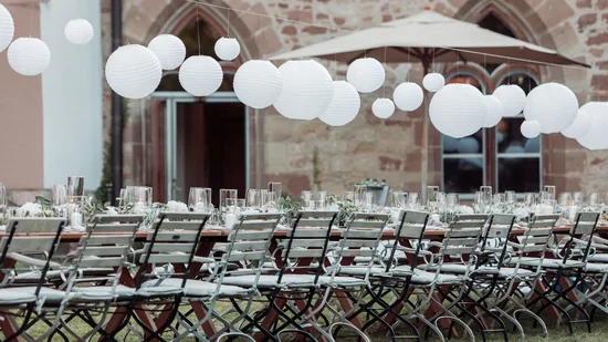 Lange gedeckte Tafel mit weißen Lampions und Stühlen im Außenbereich