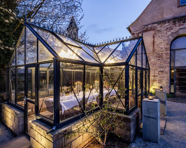 Beleuchtetes Glashaus mit festlich gedecktem Tisch im Abendlicht