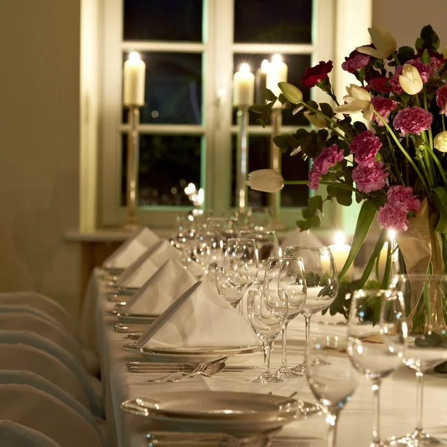 Eleganter gedeckter Tisch mit Kerzen und Blumenarrangement bei Abendbeleuchtung
