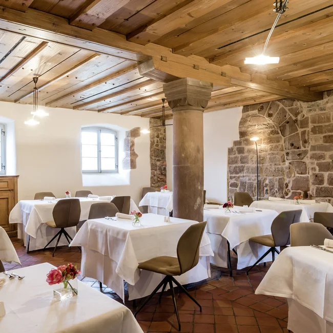 Elegantes Restaurant mit weißen Tischdecken, Holzbalkendecke und Steinmauern