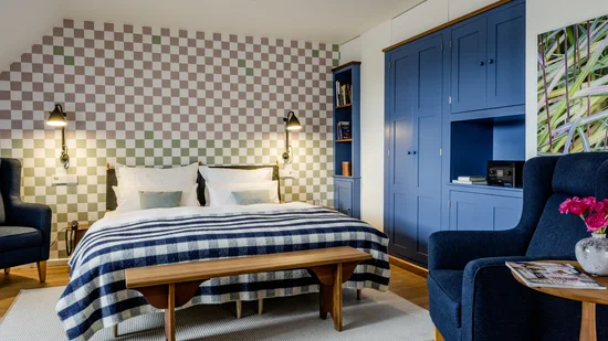 Gemütliches Schlafzimmer mit blau-weiß gestreiftem Bett, blauer Garderobe und Sessel