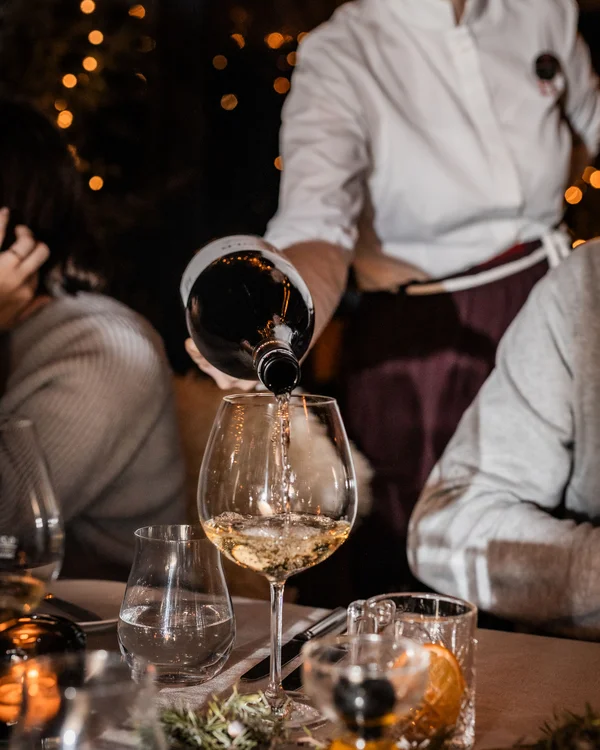 Kellner gießt Weißwein in ein Glas bei einem abendlichen Essen