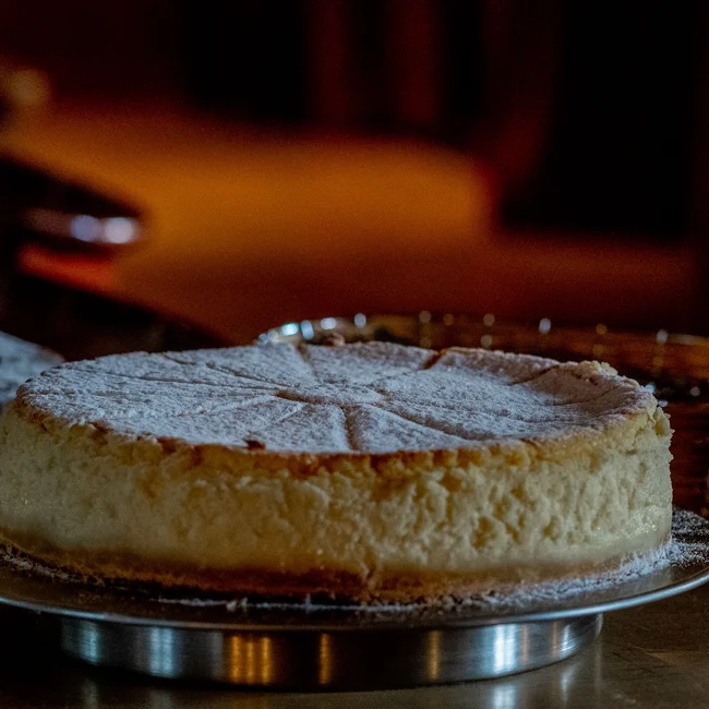 Käsekuchen mit Puderzucker auf Metallplatte in warmer Beleuchtung