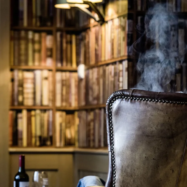 Ledersessel vor Bücherregal mit Weinflasche, Glas und Rauch im gemütlichen Raum