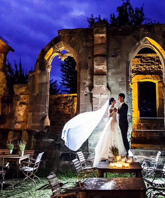 Brautpaar bei Nacht vor beleuchteten historischen Ruinen und Tischen