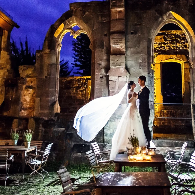 Brautpaar bei Nacht vor beleuchteten historischen Ruinen und Tischen