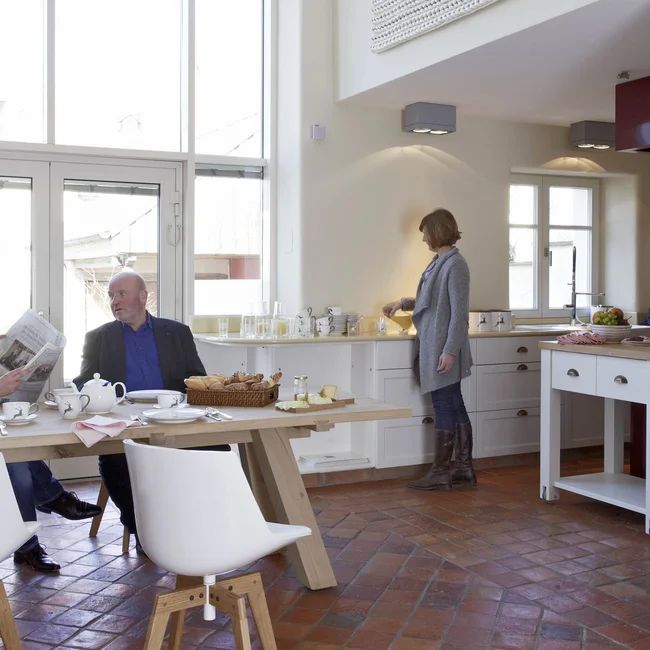 Drei Personen beim Frühstück in einer modernen, hellen Küche mit großem Fenster