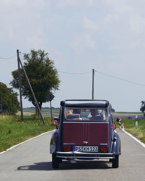 Rotes Retro-Auto fährt auf Landstraße mit grünen Feldern und Bäumen