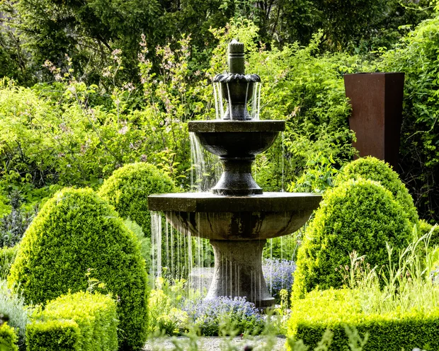 Steinbrunnen mit Wasser im gepflegten grünen Garten