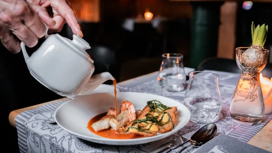 Hand gießt Sauce aus Kanne über Gourmetgericht in weißem Teller im Restaurant