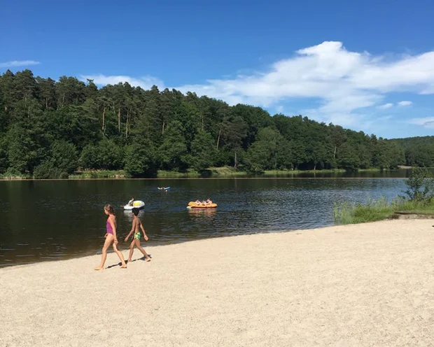 Kinder laufen am Sandstrand eines Sees mit Menschen auf Booten im Wasser