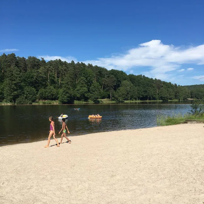 Kinder laufen am Sandstrand eines Sees mit Menschen auf Booten im Wasser