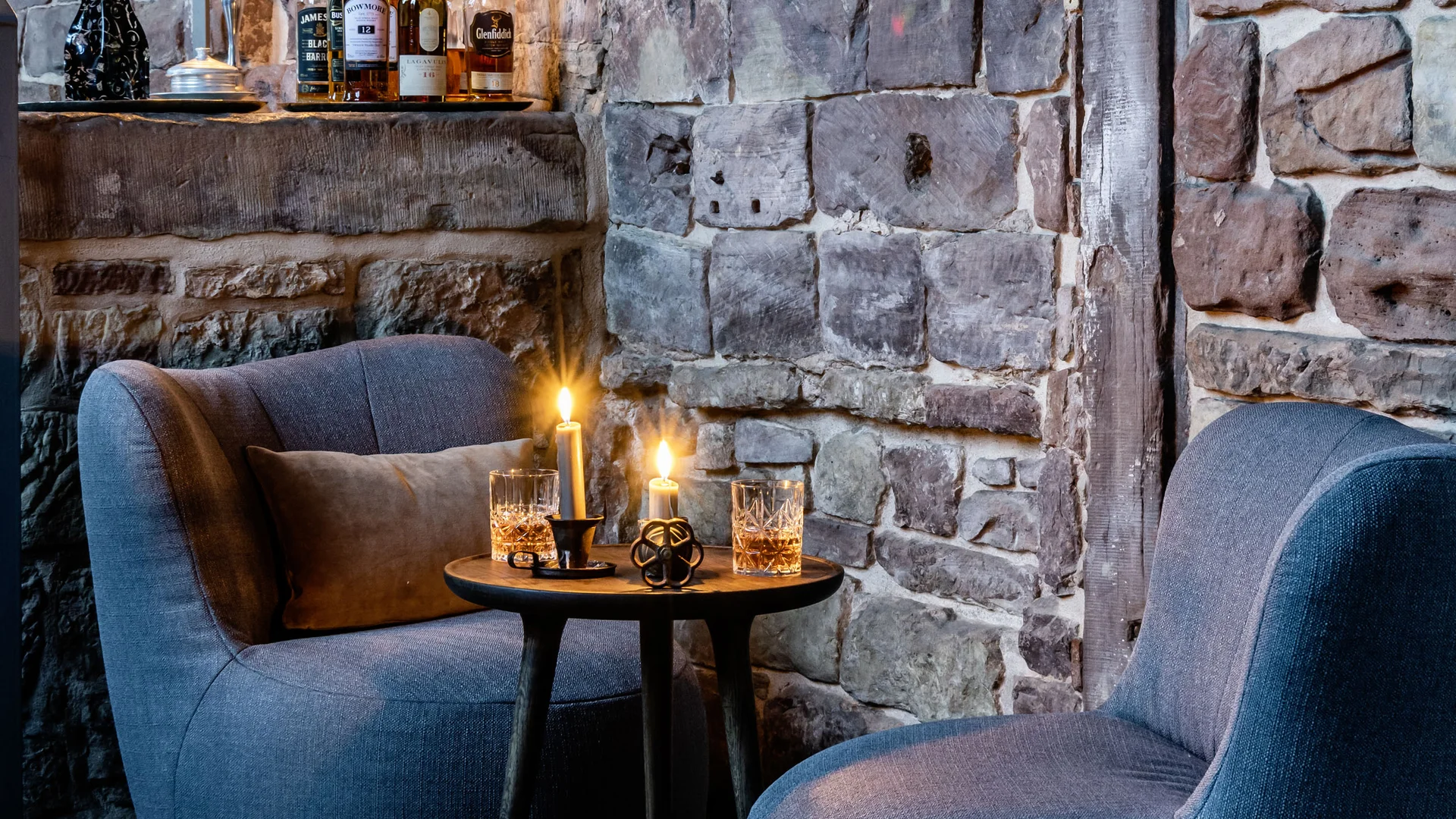 Gemütliche Sitzecke mit Kerzenlicht und Flaschen vor einer Steinwand