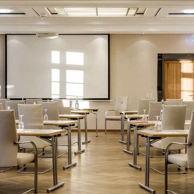 Heller Konferenzraum mit weißen Stühlen, Tischen und Projektionsleinwand