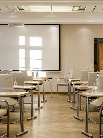 Heller Konferenzraum mit weißen Stühlen, Tischen und Projektionsleinwand