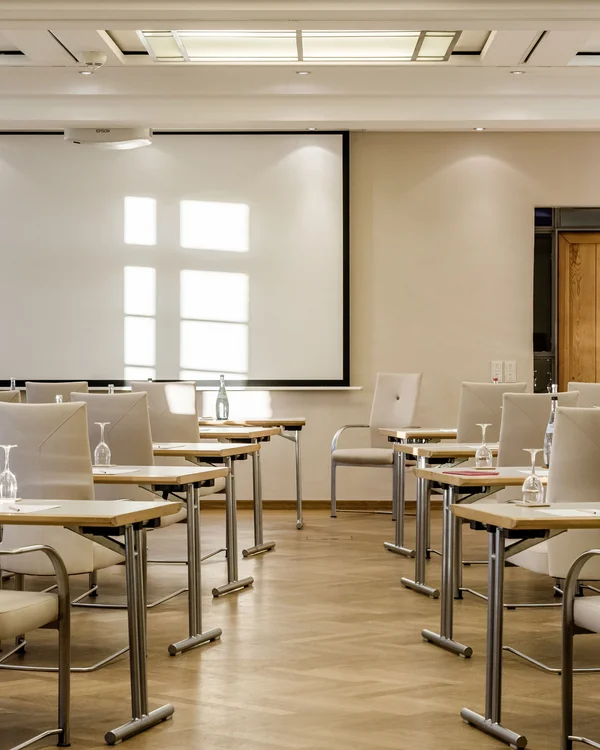 Heller Konferenzraum mit weißen Stühlen, Tischen und Projektionsleinwand