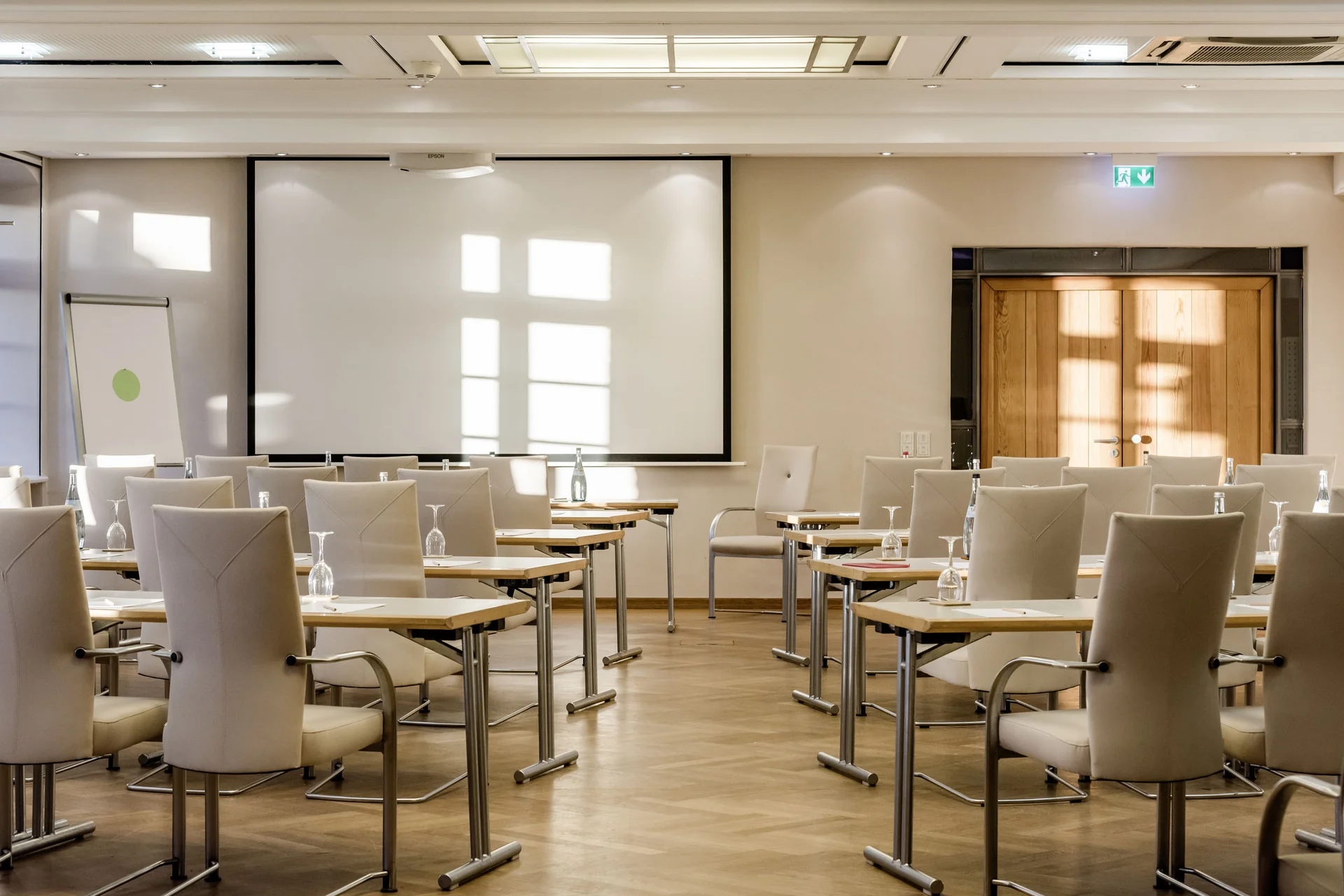 Heller Konferenzraum mit weißen Stühlen, Tischen und Projektionsleinwand