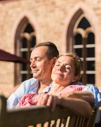Mann und Frau genießen entspannt die Sonne auf einer Bank vor einem Gebäude