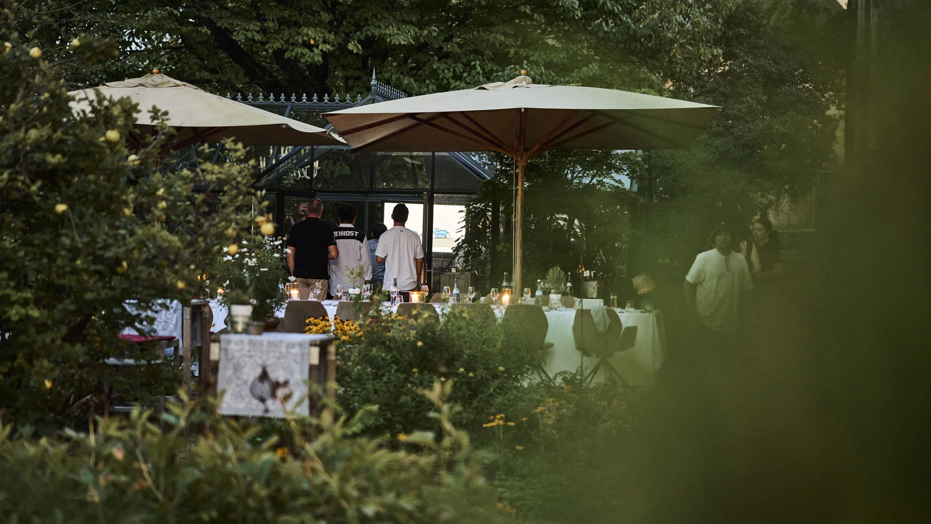 Abendessen im Garten mit gedecktem Tisch und Sonnenschirmen bei Dämmerung