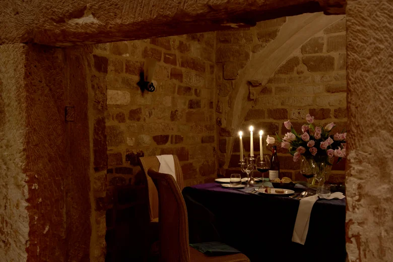 Valentinstags-Brunch Gemütliches Esszimmer mit Kerzenlicht, Wein und Blumen in einem Steingewölbe