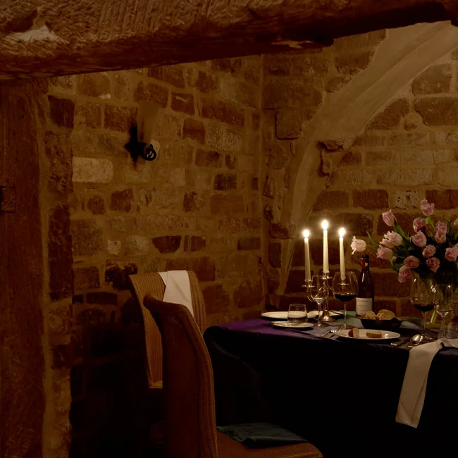 Gemütliches Esszimmer mit Kerzenlicht, Wein und Blumen in einem Steingewölbe